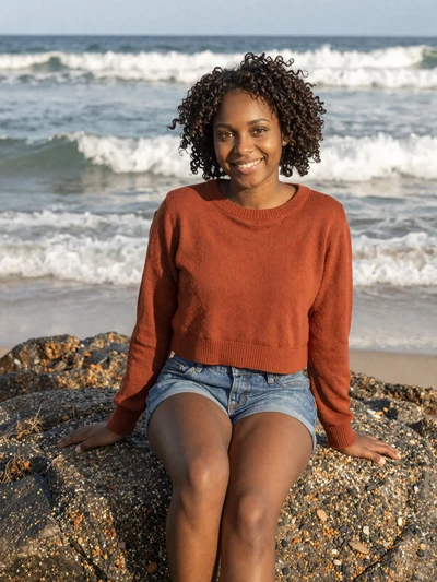 Akeela, 23, Barbadian woman from Bathsheba with curly hair sitting on beach rocks - Latin 312 verified profile